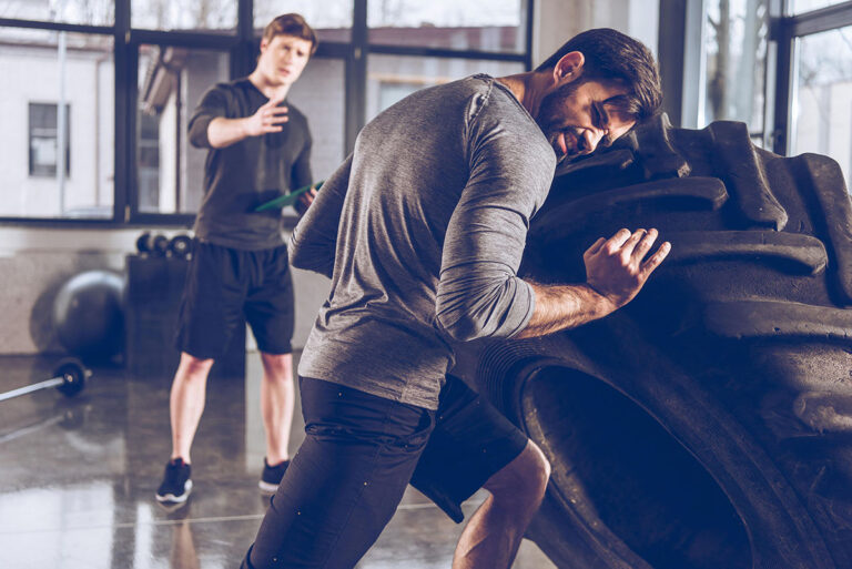 Two men working out with a large tire in a gym